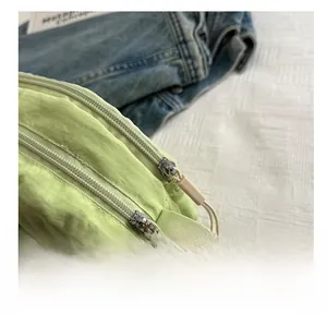 Detail view of light green nylon crossbody bag featuring a smooth two-way metal zipper