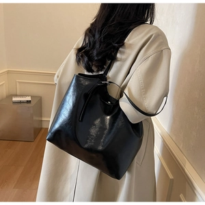 Detailed back view of a high-gloss black leather tote bag worn by a model in a cozy setting