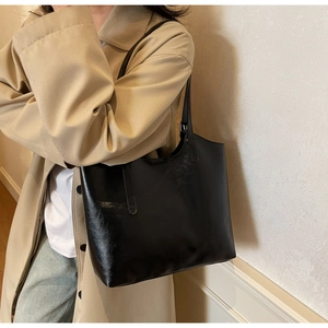 Detail of a large black glossy leather tote bag shown on model with shoulder strap