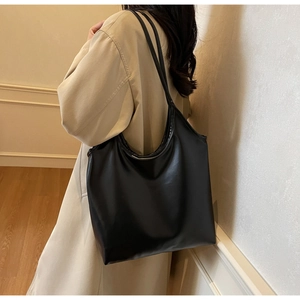 Minimalist black leather tote bag worn on shoulder showing large capacity and soft texture