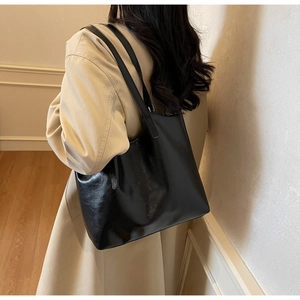 Minimalist black leather tote bag worn by a model in a cozy indoor setting