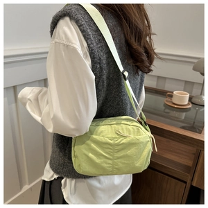 Close-up of green nylon crossbody bag with adjustable strap worn by model in a cozy room