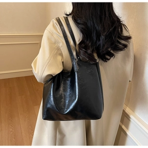 Detail of a shiny black faux leather tote bag worn with a beige coat for a commute style