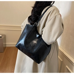 Close-up of black glossy large capacity tote bag worn over a trench coat