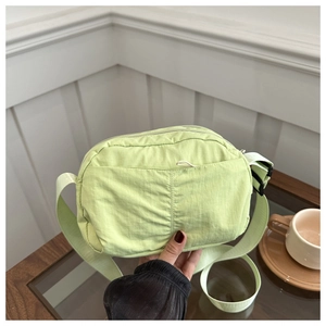 Detail of light green nylon crossbody bag with textured fabric and zipper compartment