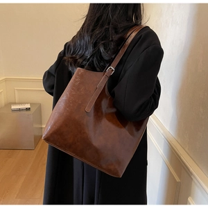Detail of vintage brown large capacity tote bag with glossy leather on model shoulder