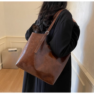 Detail of adjustable thin shoulder strap with silver buckle on brown leather tote bag