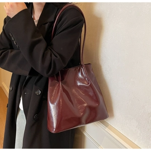 Detail of burgundy glossy leather tote bag with slim shoulder strap on model