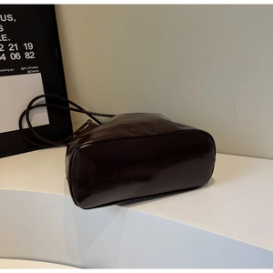 Detail of glossy dark brown tote bag with smooth reflective finish and thin shoulder strap