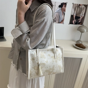 Sac cabas crème pour femme avec imprimé papillon doré et pompon dans une scène de vie