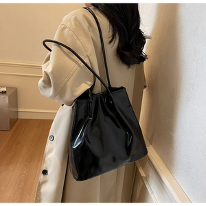 Side view of a glossy black large tote bag styled with a beige trench coat for autumn