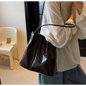 Detail of a dark brown glossy leather tote bag showing smooth texture and long straps