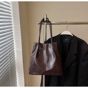 Detail view of a dark brown glossy tote bag with soft leather texture hanging on a metal rack