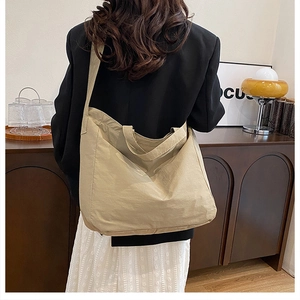 Detail view of a large beige canvas tote bag shown worn over the shoulder on a model