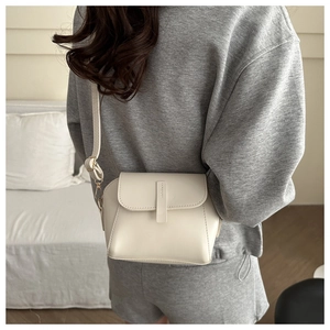 Detail of a minimalist beige crossbody shell bag with gold hardware on a casual model