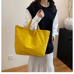 Detail view of a large yellow canvas tote bag worn by a model in a minimalist home setting