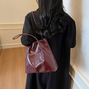 Minimalist burgundy glossy tote bag with slim shoulder straps on a model in a black coat