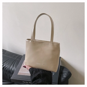 Détail d'un cabas beige brillant avec texture froissée et logo argenté gravé sur le devant
