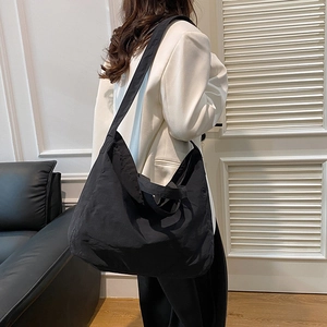 Minimalist black nylon tote bag with wide shoulder strap in spacious crossbody style