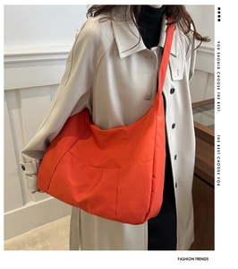 Detail view of bright orange nylon tote bag with quilted stitching on beige trench coat