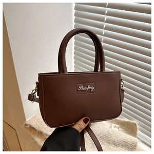 Detail of chocolate brown leather crossbody bag with metal logo and handle