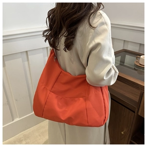 Detailed side view of a large orange nylon tote bag worn by a model for daily commute
