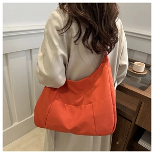 Detail of an orange quilted puffer tote bag shown on a model in a cozy indoor setting