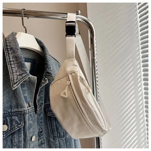 Detail of cream nylon waist bag with grid texture hanging next to denim jacket