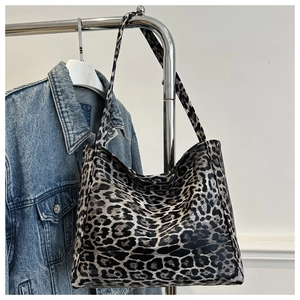 Close-up of leopard print tote bag with wide strap hanging against a denim jacket