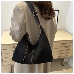 Detail of black suede shoulder bag with white contrast stitching and gold buckle hardware