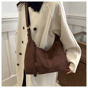 Close-up of brown suede crescent bag with white stitching and adjustable strap