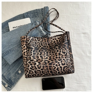 Flat lay of a leopard print tote bag with denim jacket and books on white fabric
