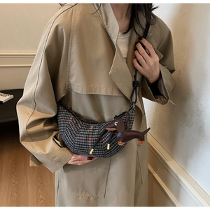 Graue Karo-Halbmondtasche mit Dackel-Anhänger aus Leder an Modell im Trenchcoat