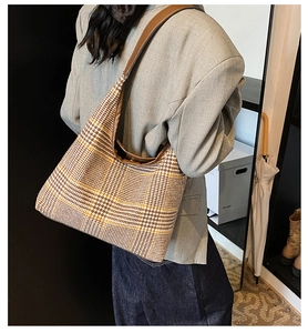 Close-up of stylish plaid hobo shoulder bag with brown leather strap on model