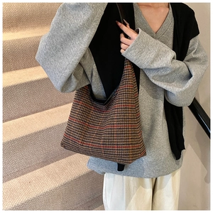 Detail of checkered shoulder bag featuring brown plaid wool fabric and black piping trim