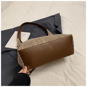 Detail of vintage plaid wool tote bag with brown leather straps on beige fabric