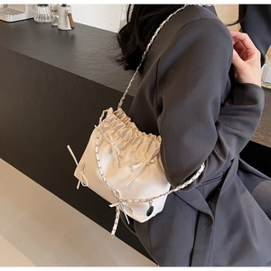 Detail of cream drawstring bucket bag with ribbons and gold-tone chain strap