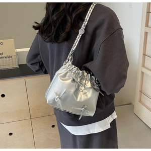 Detail of silver metallic drawstring bucket bag with bow and chain strap on a model