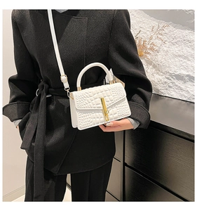 Detail of white crocodile texture leather handbag with gold bar lock on black coat