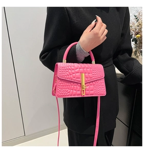 Detail of hot pink crocodile embossed handbag with gold metal clasp on a black coat