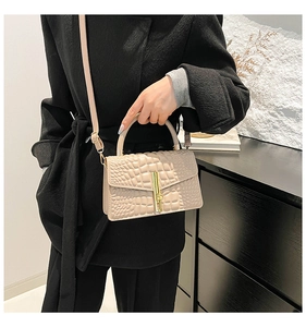 Close-up of beige faux leather handbag with crocodile pattern and golden metal clasp lock