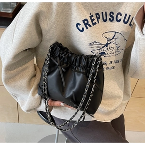 Detail of black drawstring bucket bag with leather bow and silver chain strap