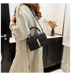Detail of black crocodile embossed crossbody bag featuring a vertical gold lock buckle
