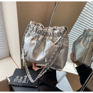 Silver metallic bucket bag with drawstring, chain strap, and bow details shown in a mirror