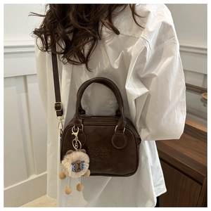 Detail of dark brown faux leather bag with Lucky LHCO Emu embossing and plush charm