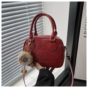 Details der roten PU-Leder Handtasche mit Struktur, Schriftzug und Plüsch-Anhänger