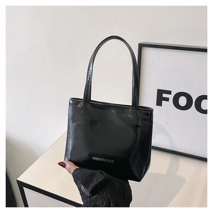 Détail d'un cabas en cuir verni noir brillant avec logo argenté et poignées fines