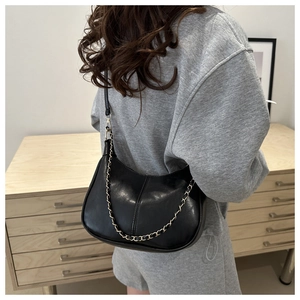 Sac sous le bras croissant noir avec chaîne dorée porté par un mannequin dans un intérieur