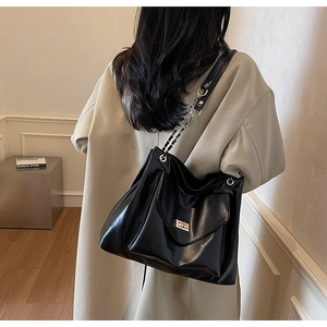 Close-up of black leather tote bag featuring a gold twist lock and elegant chain strap