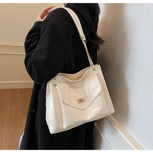 Détail d'un grand sac cabas blanc crème avec chaîne en métal sur un manteau noir